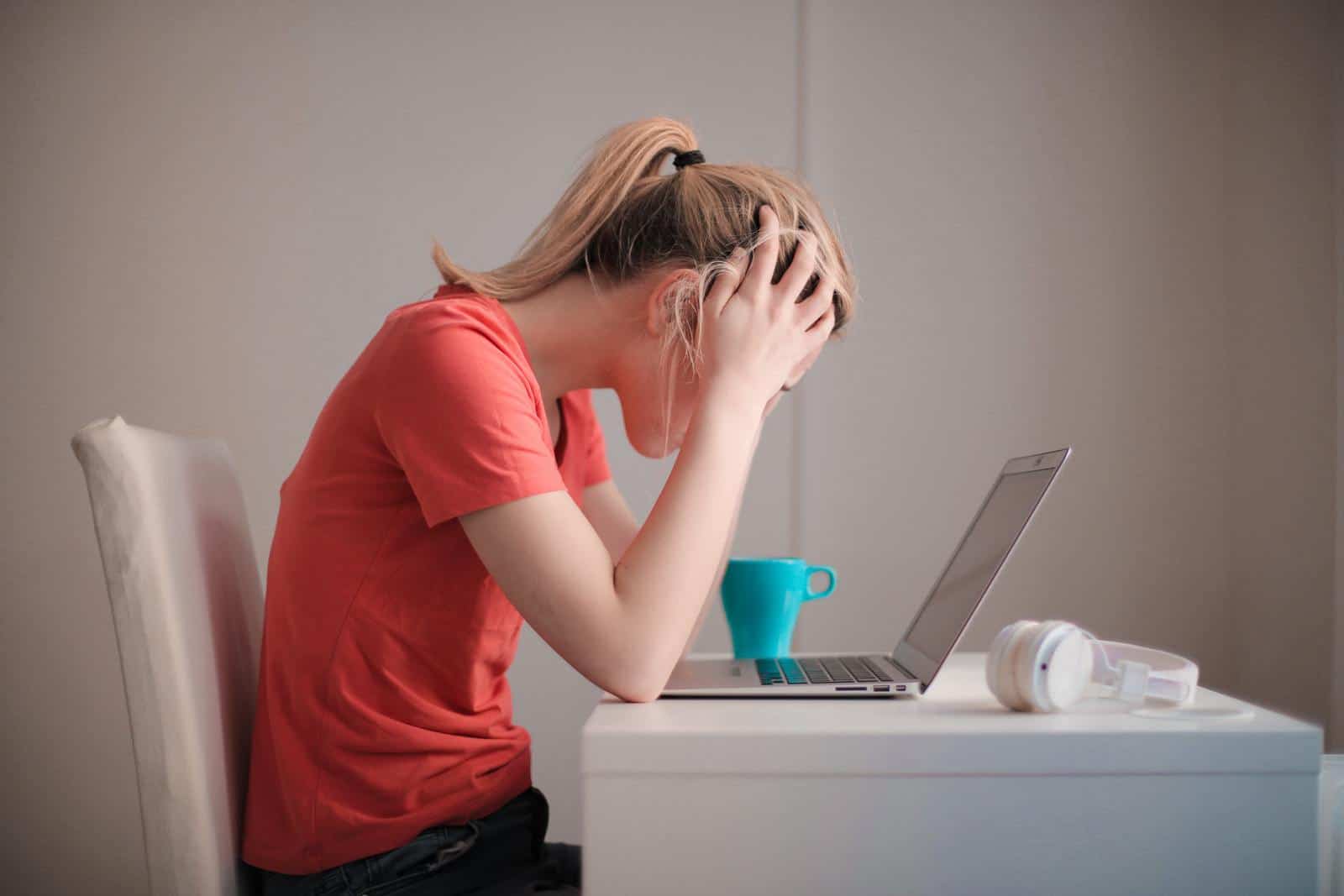 Woman holding head above laptop